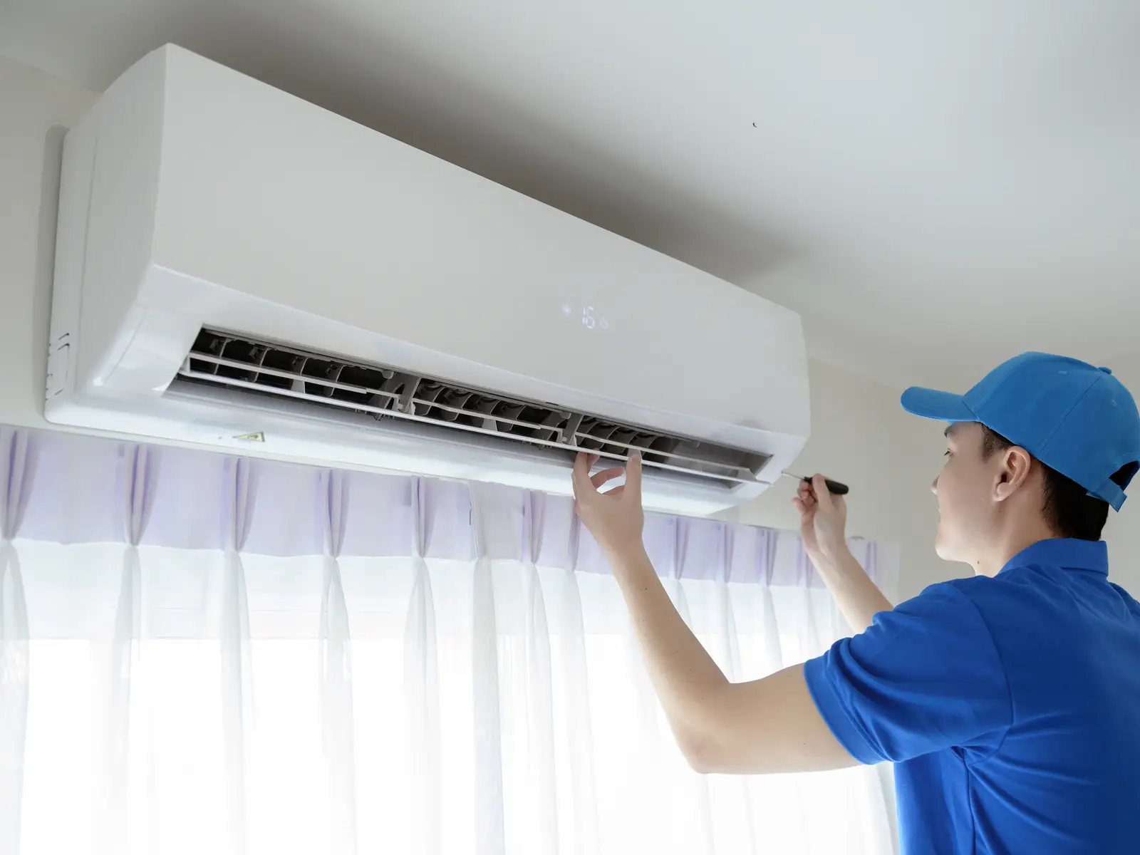 Technicien contrôlant le soufflage d'un climatiseur mural dans un local climatisé