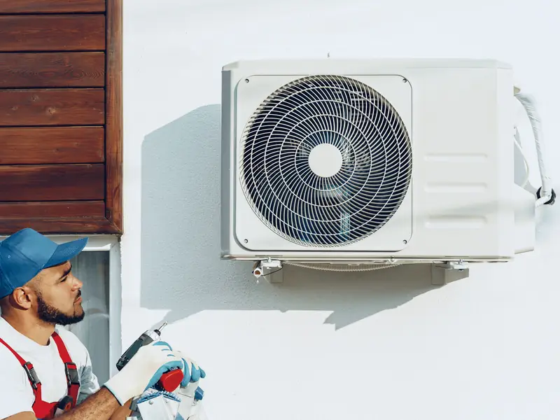 Technicien à côté d'un groupe extérieur de climatisation fixé au mur